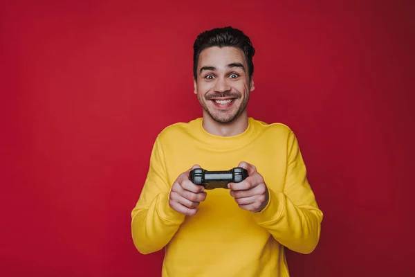 Μισό μήκος του τρελό καστανά μαλλιά τύπος κρατώντας joystick σε κόκκινο φόντο — Φωτογραφία Αρχείου