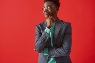 Kırmızı arka planda ayakta gözlük gülümseyen genç adam