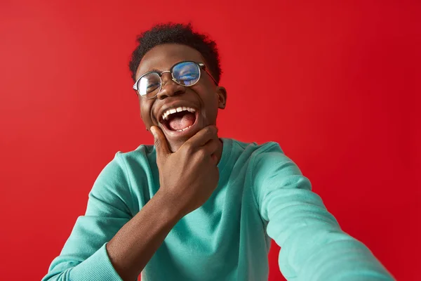 Funny Afro Amerikaanse vent in glazen poseren in Studio op rode achtergrond — Stockfoto