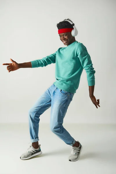 Positive young guy with red bandage is dancing in studio