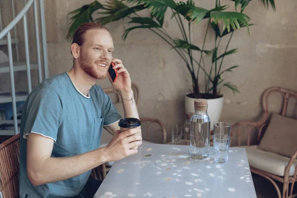 Gladlynt man pratar på mobil telefon och samtidigt ha varm dryck — Stockfoto