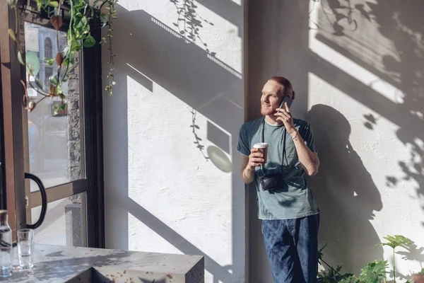 Беззаботный парень с кофе общается по телефону в помещении — стоковое фото