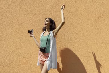 Açık turuncu duvara karşı duran retro kamera ile neşeli esmer kız