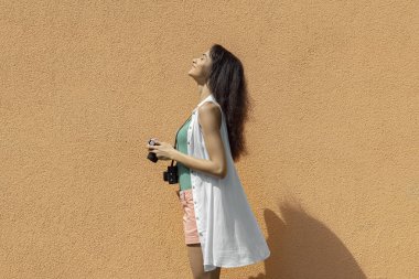 Açık turuncu duvara karşı duran retro kamera ile çekici esmer kız