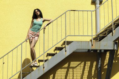 Sarı duvara karşı merdivenlerde duran güzel esmer kız