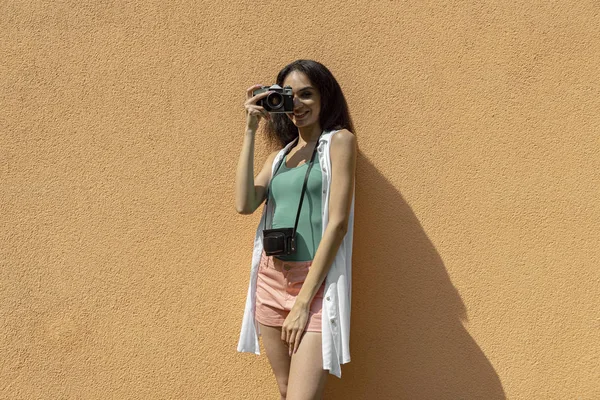 Красивая брюнетка с ретро-камерой, стоящая напротив светло-оранжевой стены — стоковое фото