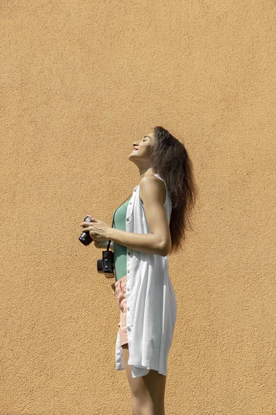 Γοητευτική μελαχρινή κορίτσι με ρετρό κάμερα στέκεται ενάντια φως πορτοκαλί τοίχο — Φωτογραφία Αρχείου