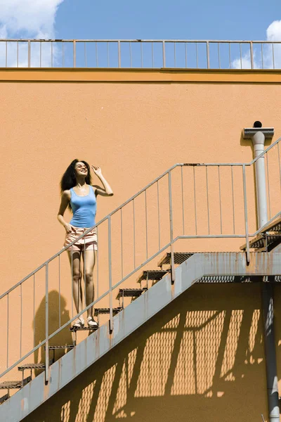 Schöne junge Frau steht auf Treppen gegen orangefarbene Wand — Stockfoto