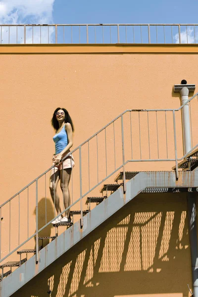 Привлекательная молодая женщина стоит на лестнице напротив оранжевой стены — стоковое фото
