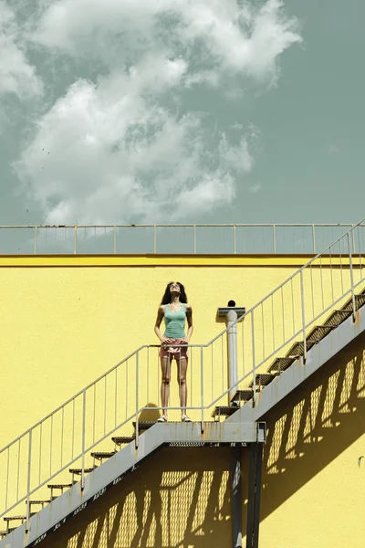 Sarı duvara karşı merdivenlerde duran büyüleyici genç kadın