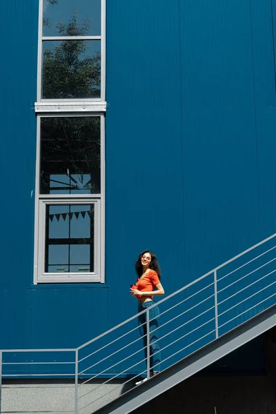 Όμορφη νεαρή κυρία στέκεται στις σκάλες ενάντια στον μπλε τοίχο — Φωτογραφία Αρχείου