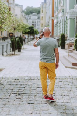 Gri saçlı olgun adam şehirde cadde boyunca yürüyor