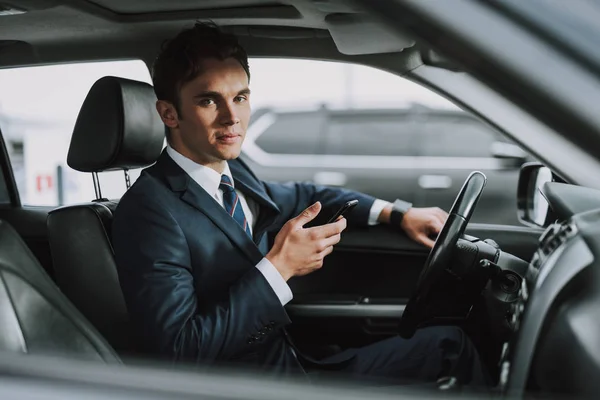 Joven hombre guapo sosteniendo el teléfono móvil en su coche — Foto de Stock
