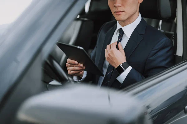 Jovem bonitão de terno sentado em seu carro com tablet — Fotografia de Stock