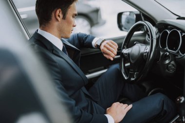 Arabasında oturan ve saatine bakan genç adam