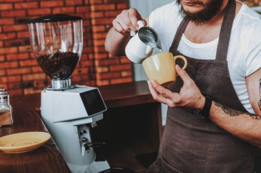 Sakallı barista ayakta ve fincan içine süt dökme