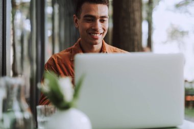 Neşeli genç adam masada oturan ve dizüstü bilgisayar kullanarak