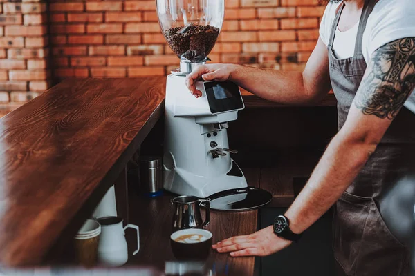 Татуированный бариста кладет одну руку на кофемолку — стоковое фото