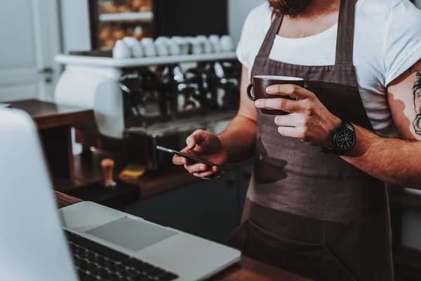 Barista debout avec du café et en utilisant un smartphone moderne — Photo