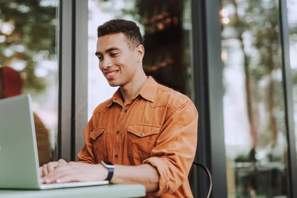 Jovem alegre em camisa laranja usando laptop — Fotografia de Stock