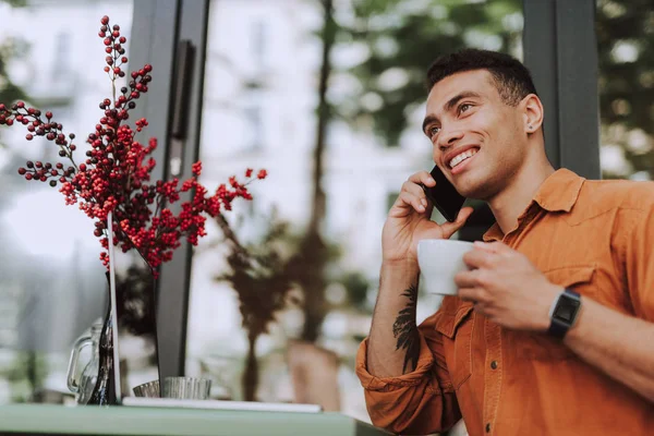 Glad ung man med kopp kaffe talar på mobiltelefon — Stockfoto