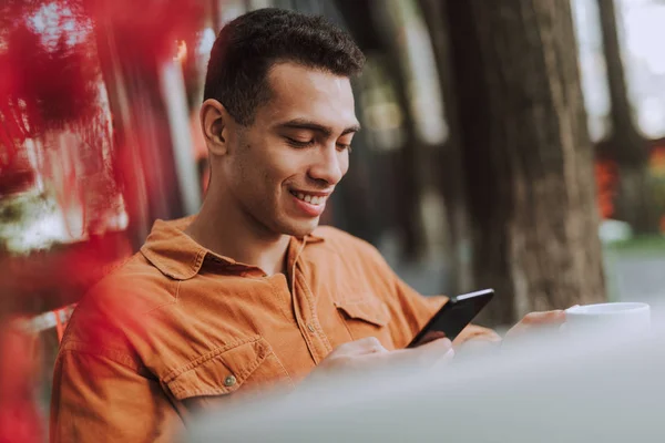 Glad ung man i orange skjorta med mobiltelefon utomhus — Stockfoto