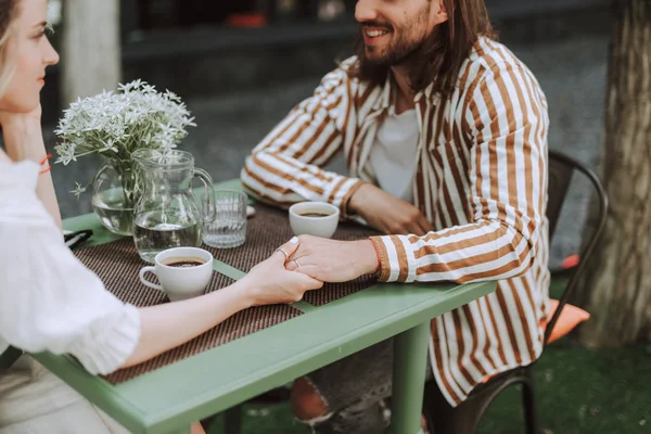 Verliebtes Paar sitzt mit Tassen Kaffee am Tisch und hält Händchen — Stockfoto