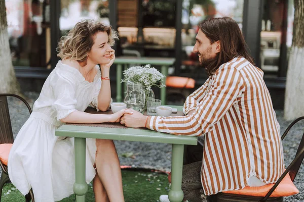 Красивая пара, сидящая за столом и держась за руки в кафе на открытом воздухе — стоковое фото