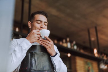 Siyah önlüklü yakışıklı genç adam kahve içiyor