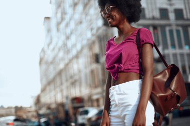 Afro-Amerikalı bayan sokakta bir kenara bakarak ve gülümseyerek