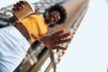 Şehirde sıcak içecek tutan afro-Amerikan kadın similing