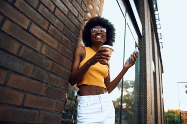 Mutlu genç kadın tuğla duvara yakın kahve tutan