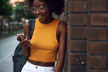 Mutlu Afro-Amerikan Bayan çanta tutarak Smartphone ve ayakta açık havada