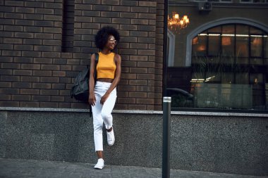 Tuğla duvara yakın dinlenmek olan gülümseyen afro-amerikan kadın