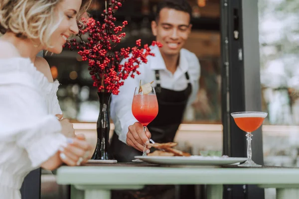 Barman serwujący napój dla młodej kobiety w kawiarni na świeżym powietrzu — Zdjęcie stockowe