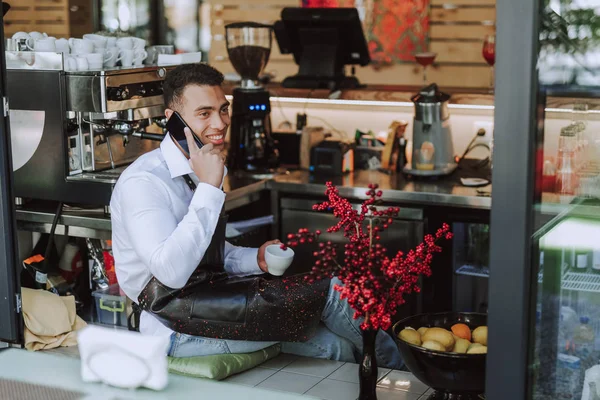 Beau barman avec boisson chaude parlant sur téléphone portable dans le café — Photo