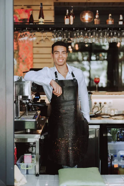 Beau barman en tablier noir debout dans un café — Photo