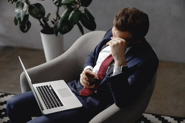 Hombre de negocios cansado sentado en sillón con portátil y whisky — Foto de Stock