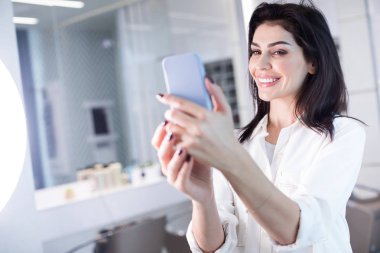 Kuaför salonu kollarında cep telefonu ile gülümseyen bayan düşük açı