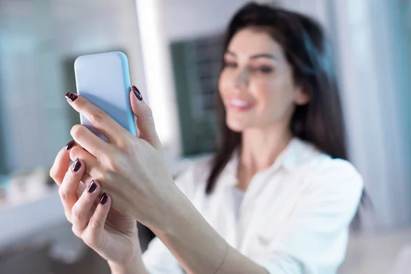 Señora sonriente sosteniendo el teléfono celular en brazos en la peluquería — Foto de Stock