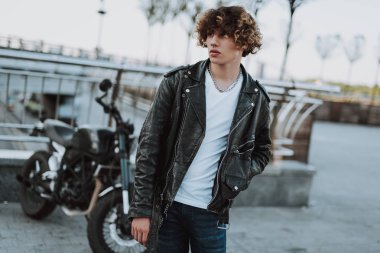 Deri ceketli kıvırcık genç adam uzağa bakıyor