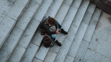 Ceket ve çizmetaş merdivenlerde oturan kıvırcık genç adam