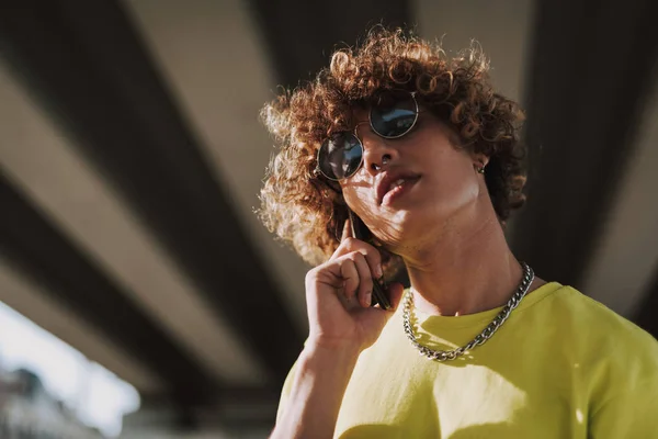 Calm curly young man in sunglasses talking on the phone