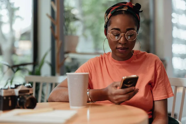 Jonge Afro-Amerikaanse vrouw met behulp van smartphone in café — Stockfoto