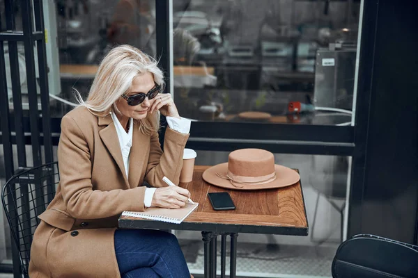 Mulher madura fazendo anotações em café foto stock — Fotografia de Stock