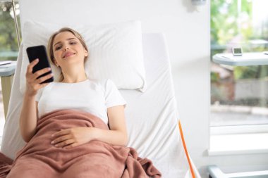 Hastane odasında cep telefonu kullanan gülümseyen genç bayan