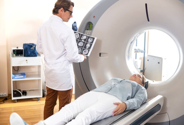 Radiology technologist holding brain CT scan and looking at patient