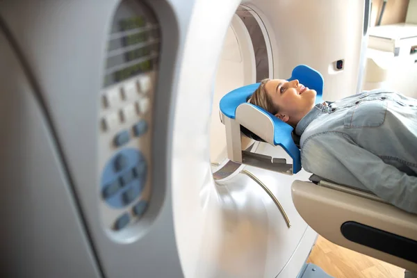 Mujer joven sonriente acostada en la mesa de la máquina de TC en la clínica de radiología —  Fotos de Stock