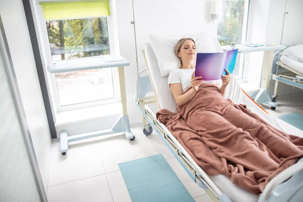 Charmante Dame liegt im Bett und liest in moderner Klinik — Stockfoto