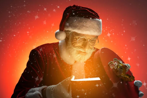 Papai Noel olhando para a caixa de presente com luz mágica — Fotografia de Stock